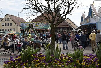 belebter Schrannenplatz hinter Blumenbeet