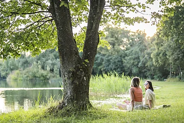 Zwei Frauen liegen auf einer Decke am Leitnerweiher, auch Weicheringer See genannt, und unterhalten sich.