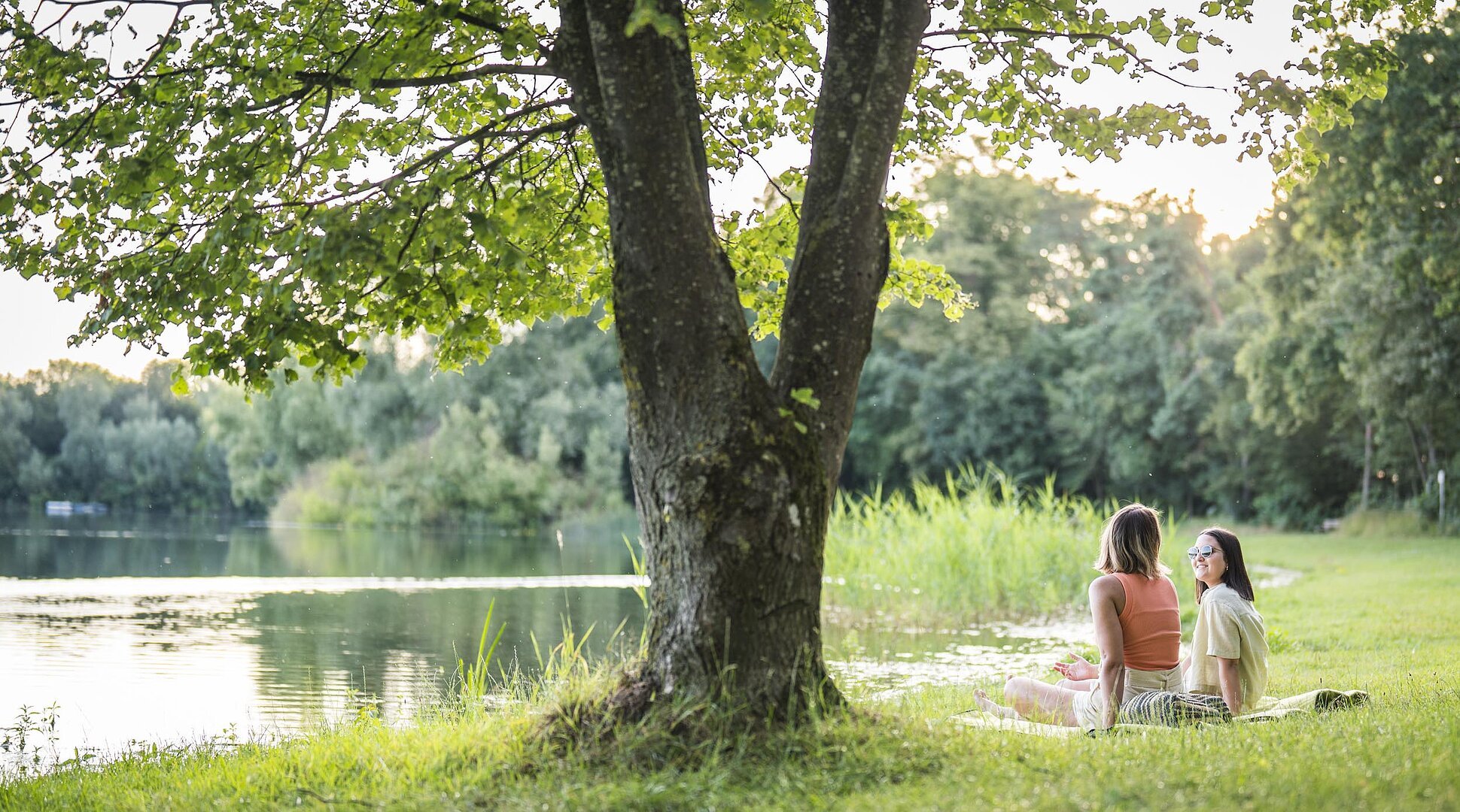 Zwei Frauen liegen auf einer Decke am Leitnerweiher, auch Weicheringer See genannt, und unterhalten sich.