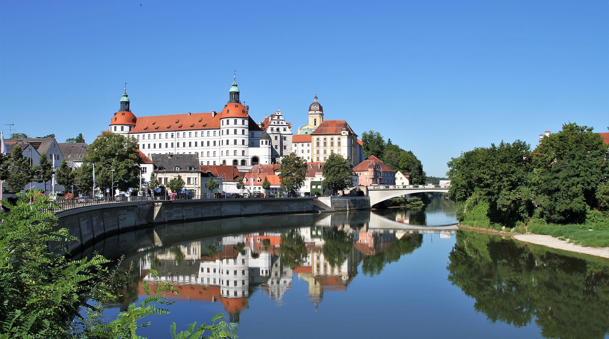 Stadtansicht mit Schloss und Brücke, Spiegelung im Fluss, blauer Himmel, Bäume am Ufer