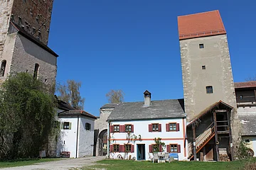 Bauernhof mit weißen Gebäuden, zwei Türmen und Gartenmöbeln unter blauem Himmel.