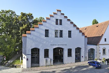 Gebäude mit Treppengiebel und Schriftzug Tourist-Information, davor gepflasterte Straße und blauer Pkw.