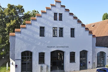 Gebäude mit Treppengiebel und Schriftzug Tourist-Information, davor gepflasterte Straße und blauer Pkw.