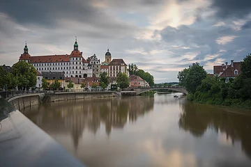 Fluss mit Brücke und historischen Gebäuden im Hintergrund, bewölkter Himmel.