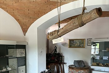 Rathauskeller Burgheim In einem gemauerten Gewölbe stehen Vitrinen an den Wänden. Von der Decke hängt ein alter Balken