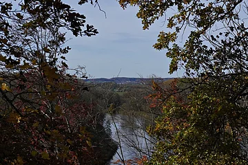 Fluss fließt durch herbstlichen Wald mit bunten Blättern unter blauem Himmel.