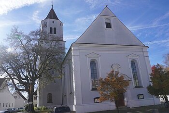 Kirche mit Turm und Bäumen im Vordergrund bei sonnigem Himmel und blauem Hintergrund.