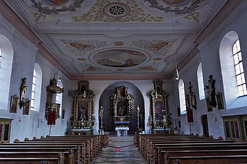 Innenraum einer Kirche mit bemaltem Gewölbedecke, Holzbankreihen und Altären mit religiösen Figuren und Gemälden