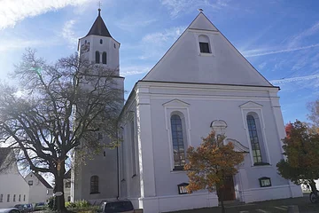Kirche mit Turm und Bäumen im Vordergrund bei sonnigem Himmel und blauem Hintergrund.