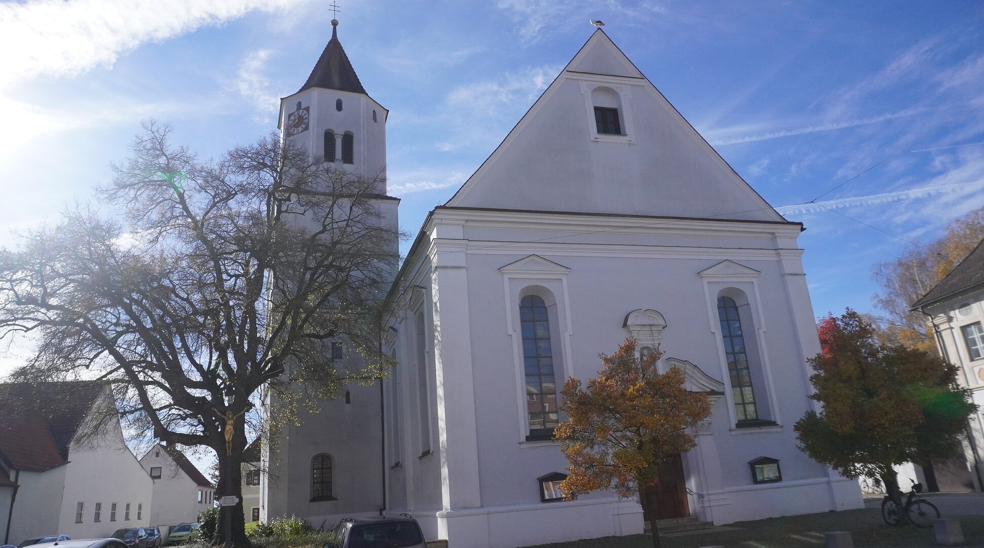 Kirche mit Turm und Bäumen im Vordergrund bei sonnigem Himmel und blauem Hintergrund.