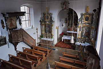 Innenraum einer kleinen Kirche mit Holzbänken, Kanzel, Altären und religiösen Gemälden an den Wänden.